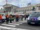 Aktivist:innen der Letzten Generation blockieren einen Zebtrastreifen vor dem Parlament in Wien. Rechts und hinten im Bild stehen Polizist:innen und Polizeiwägen.